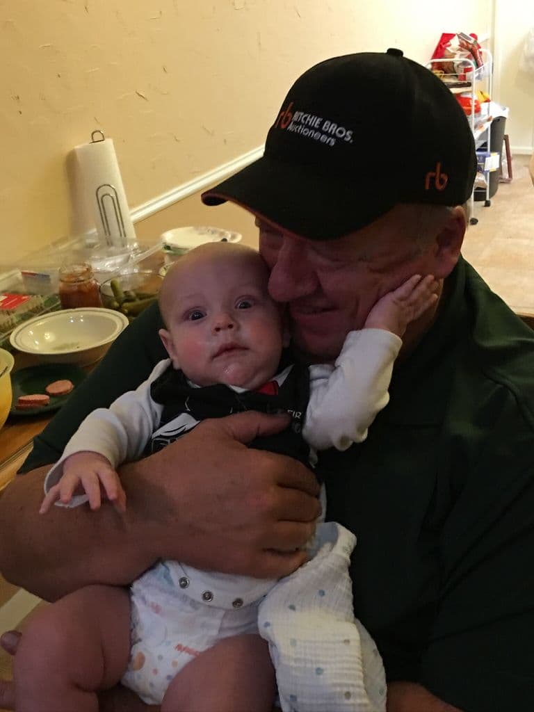 Ernie in a ball cap, cradling a baby