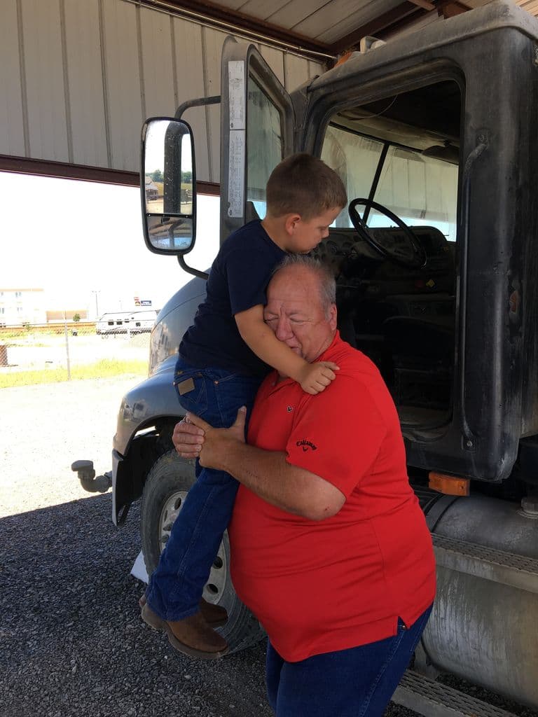 Ernie lifting a young boy up for a hug beside a truck