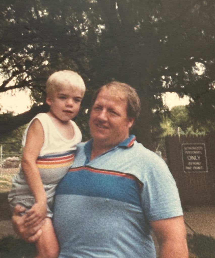 A younger Ernie outdoors, holding a small child on his arm